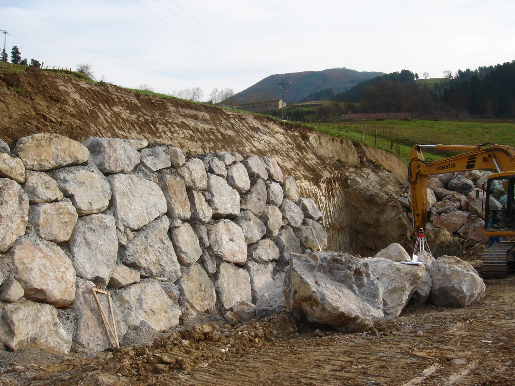 Large fitted natural boulder retaining wall on sloping site, construction equipment visible
