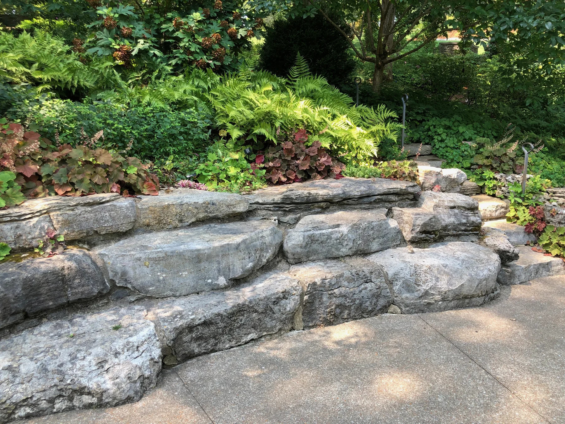 Large layered stone retaining wall, lush planted bed and curved walkway